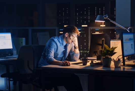 A male employee who has his hands on his head and is stressed at a computer