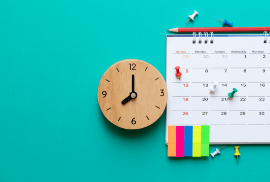 A clock and a wall calendar hung up on a turquoise wall