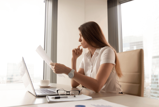 A woman in her office sitting at her desk looking at a document