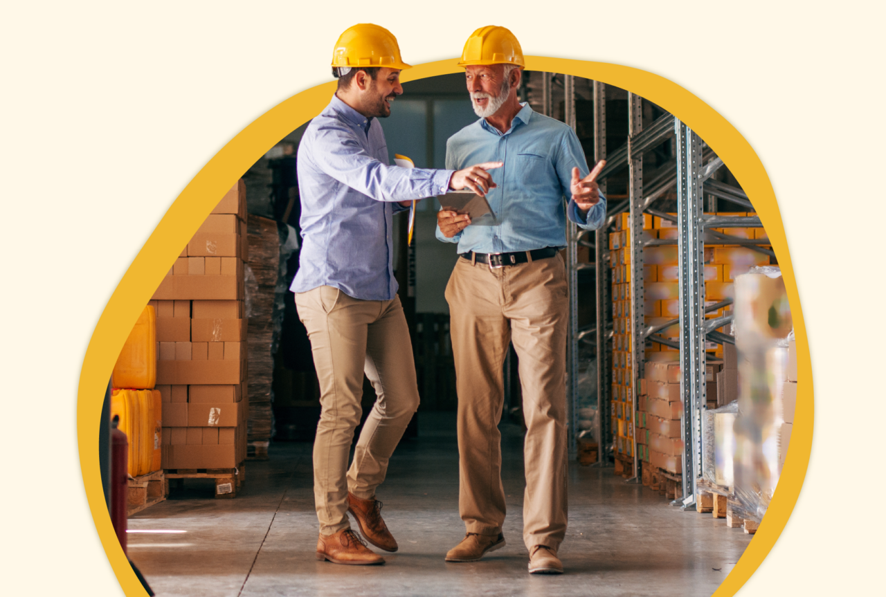 Two men in a warehouse wearing hard hats talking