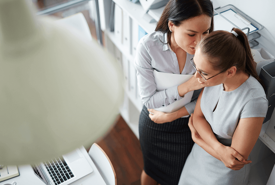 Two female employees in a room and one is whispering something in the other ones ear