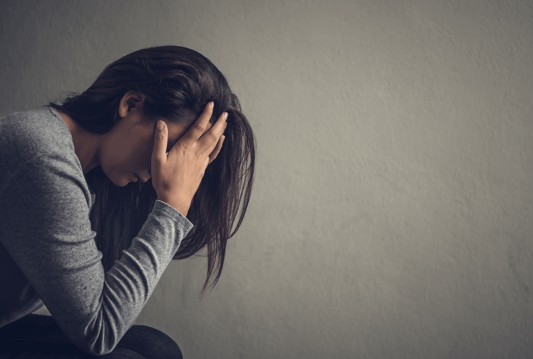 A woman in a corner with her head in her hands looking at the floor