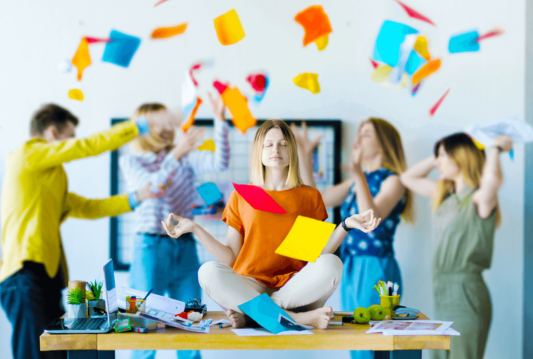 4 Employees throwing papers in the air and one employee on desk trying to meditate